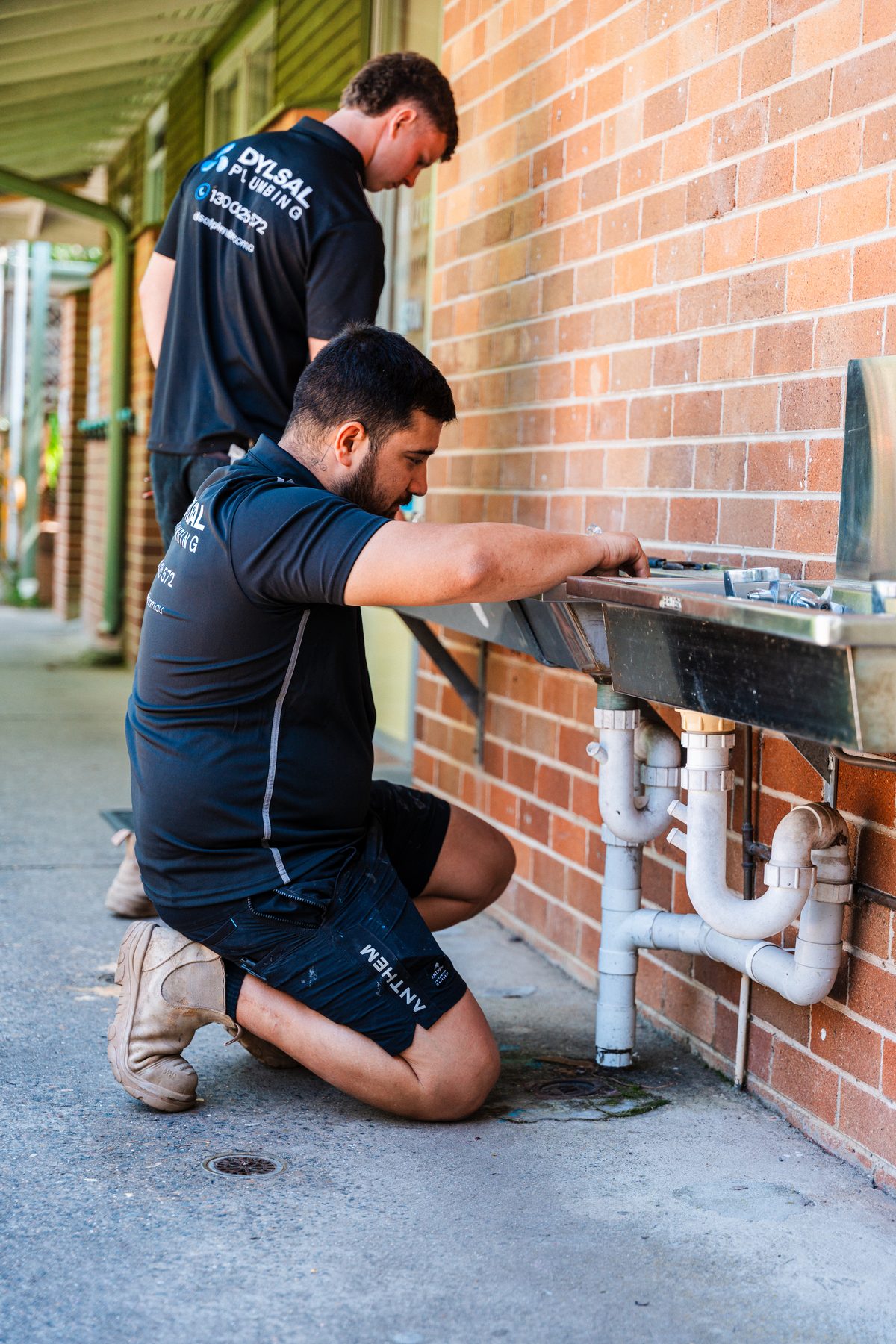 DYLSAL plumber working on outdoor brick wall pipework